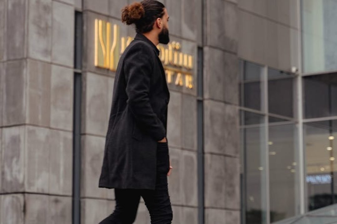 Fashionable man in dark attire walking amidst urban architecture in Mashhad, Iran.